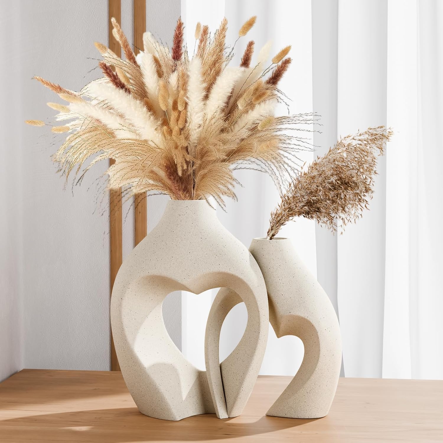 Two white abstract vases with dried pampas grass on a wooden surface.