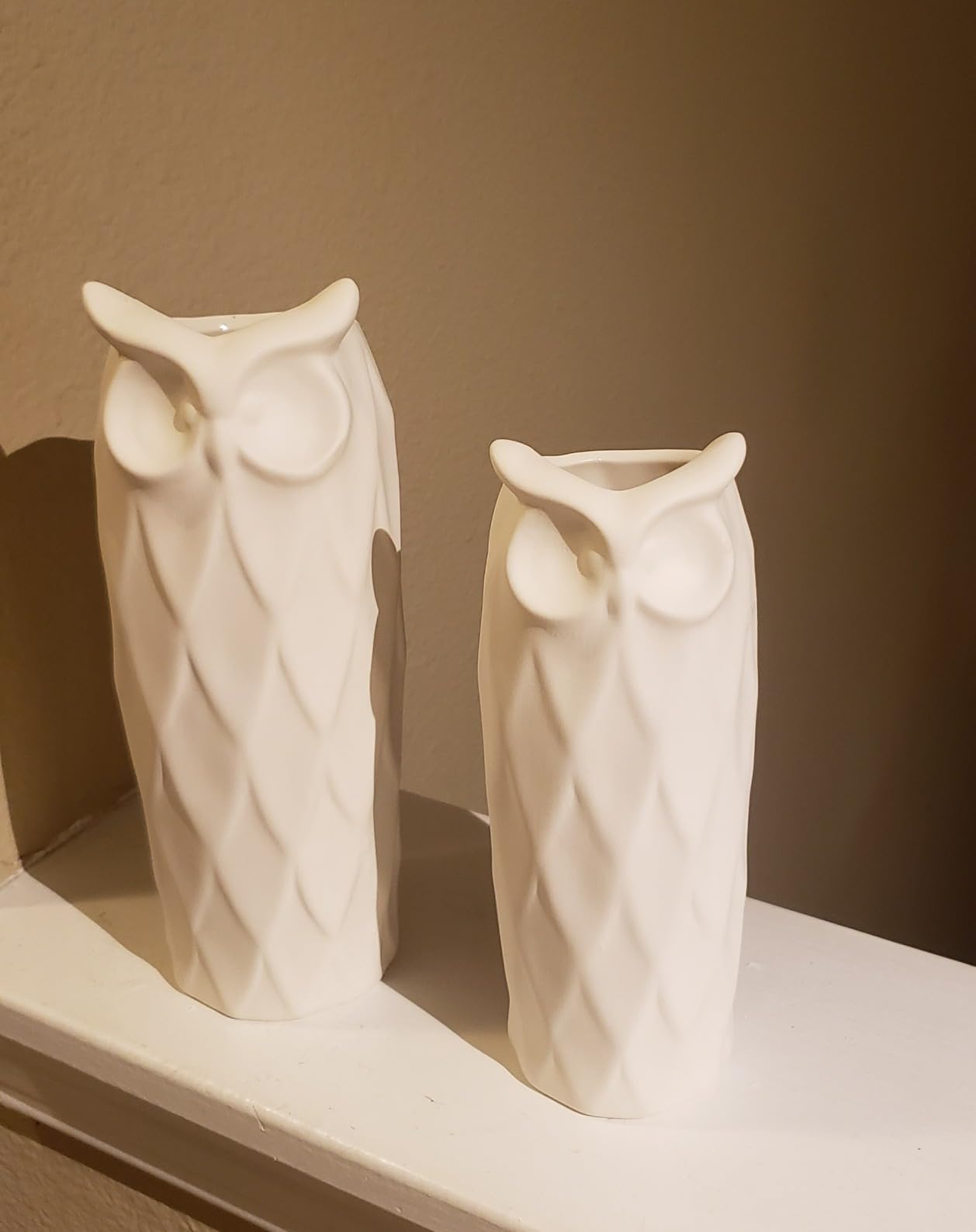 Two white owl-shaped vases on a shelf against a brown wall.