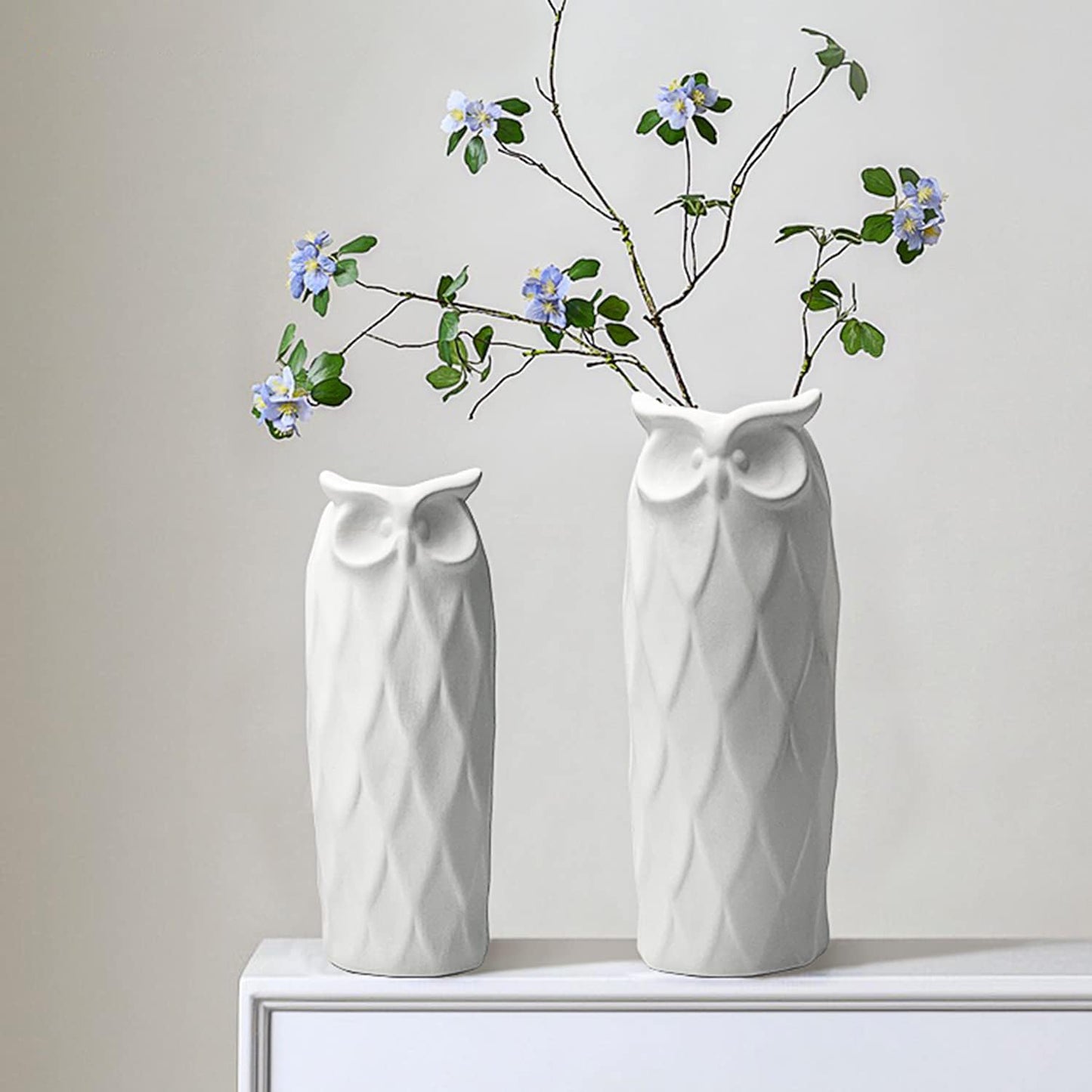 Two white owl-shaped vases with branches and flowers on a light background
