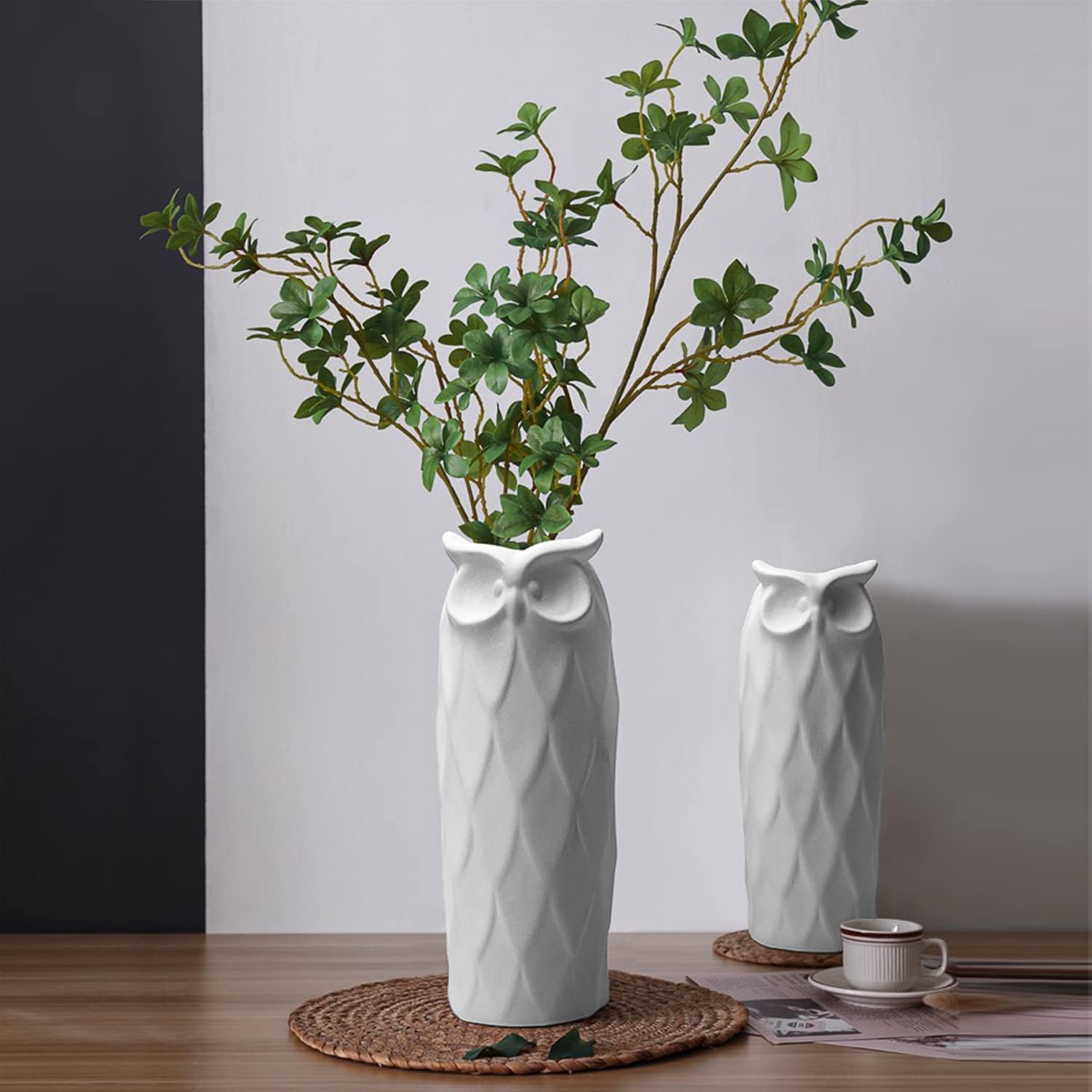 Two white owl-shaped vases with green branches on a wooden surface.