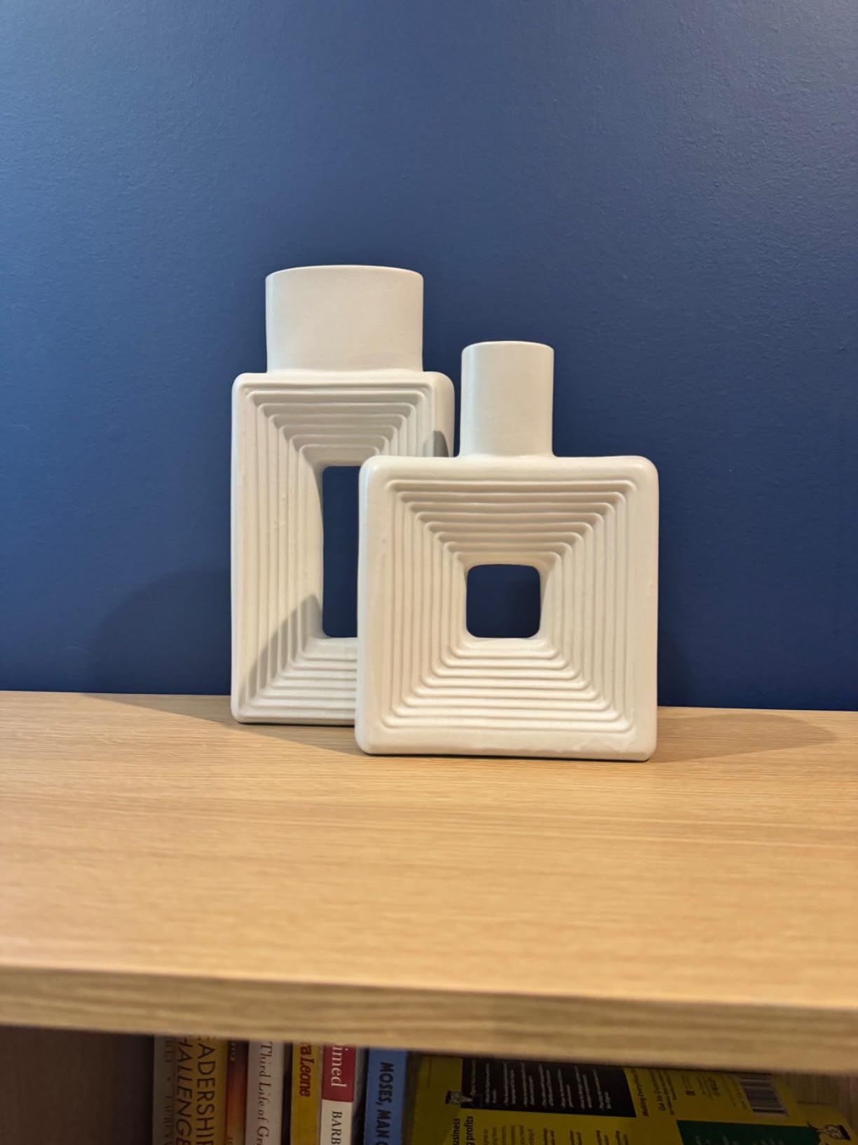 Two white square-shaped vases on a wooden surface with a blue wall background