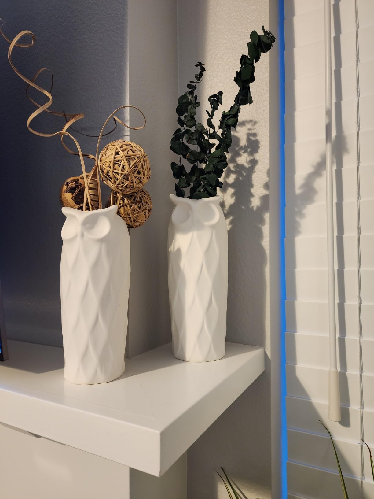 Two white textured vases with decorative elements on a shelf next to a tiled wall.