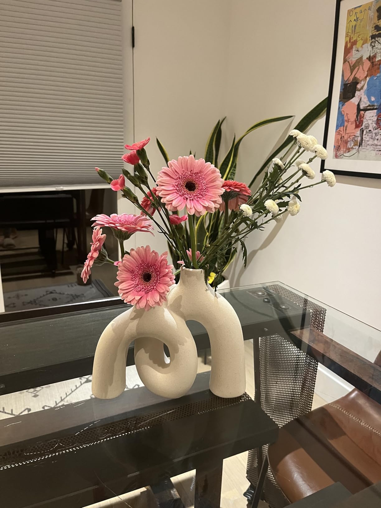Two white vases with pink flowers on a glass table.