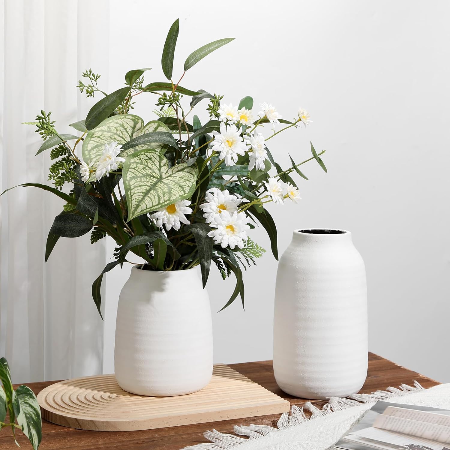 Two white vases with plants on a wooden surface against a light background