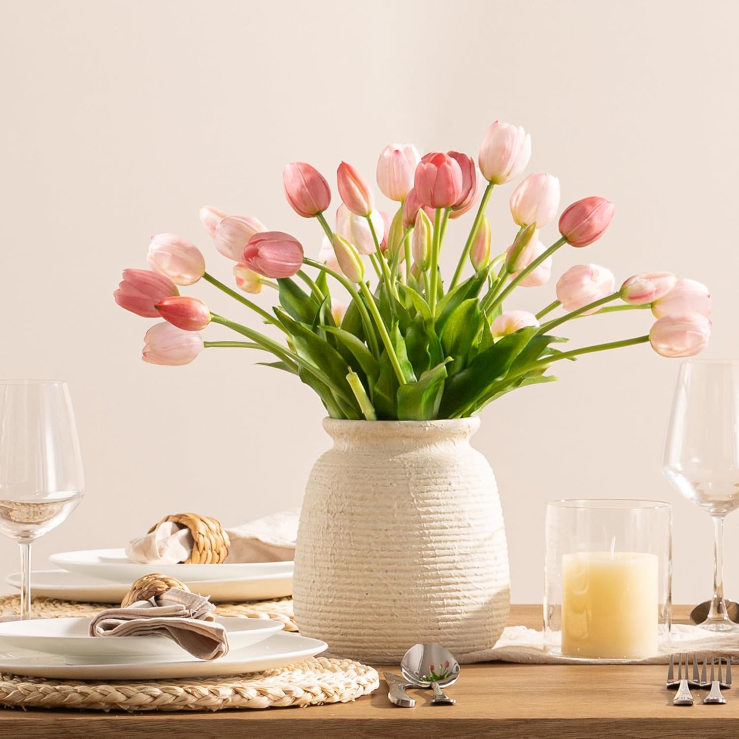 Vase of pink tulips on a table setting with plates, glasses, and candles.