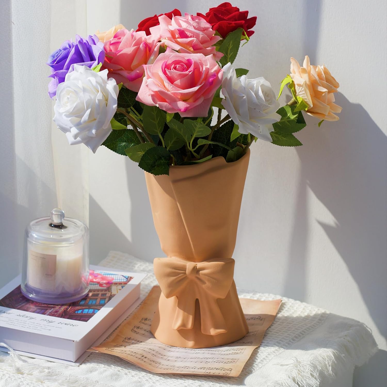 Vase with colorful artificial flowers on a table with a candle and book