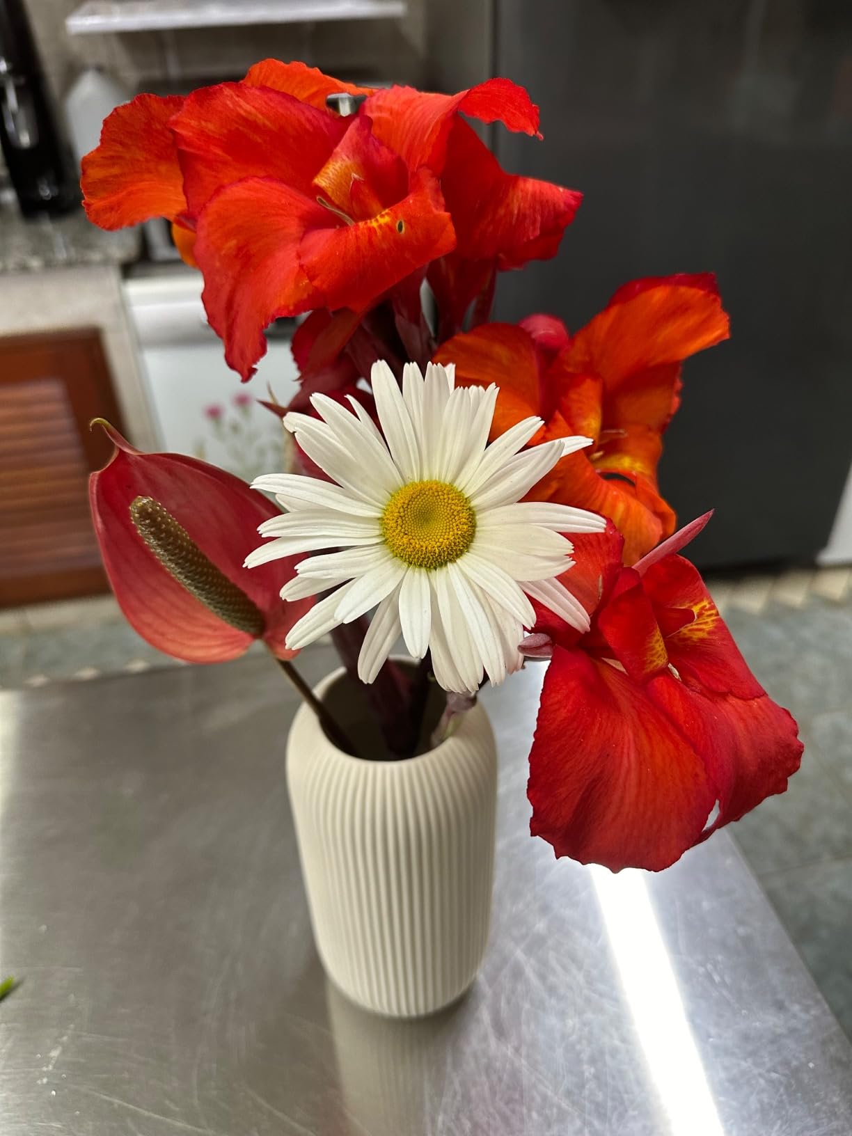 Vase with red flowers and a white flower on a reflective surface