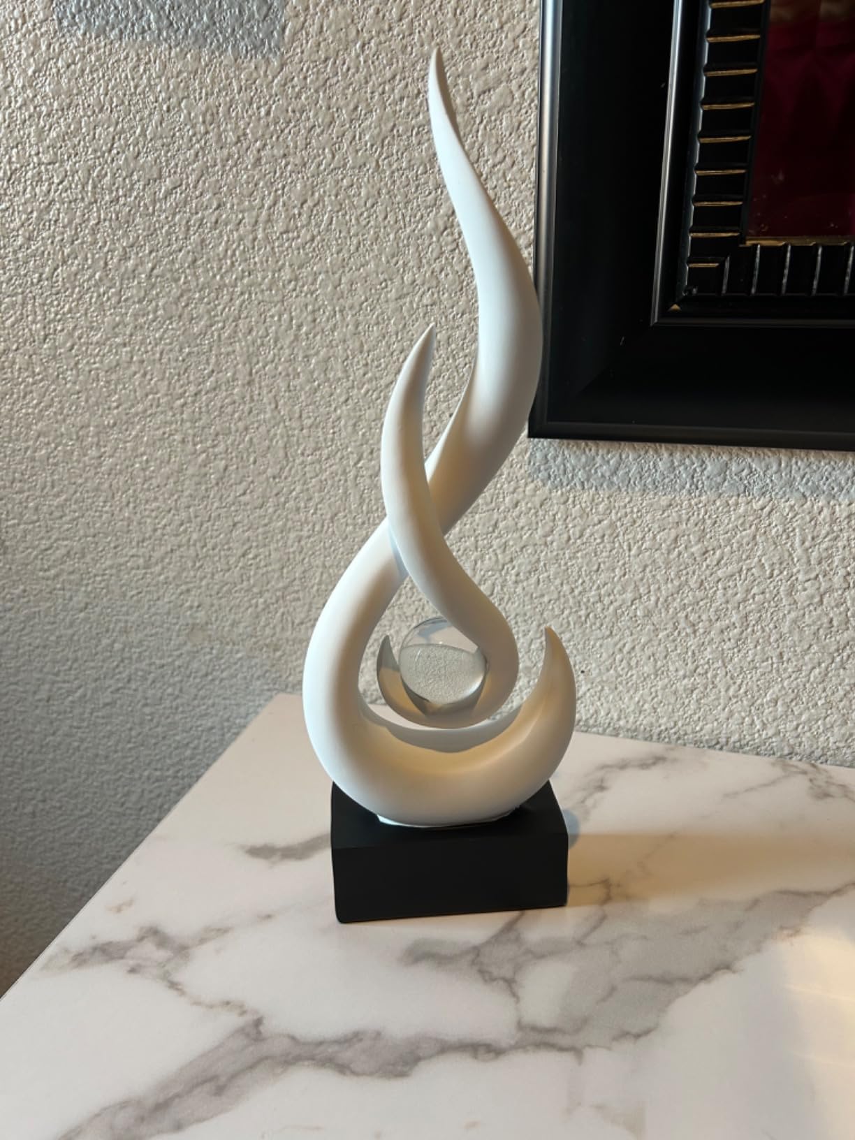 White abstract sculpture on a black base against a textured wall.