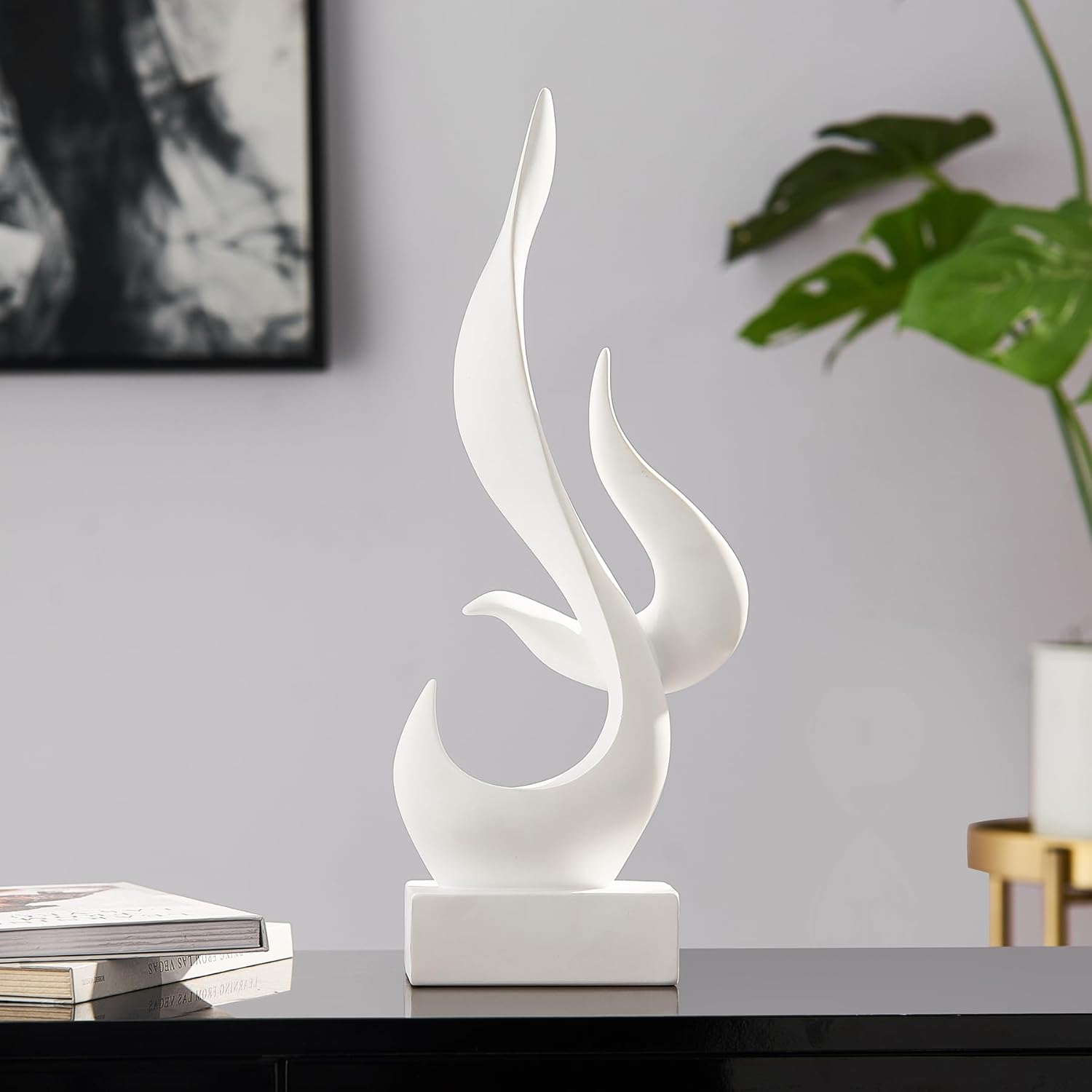 White abstract sculpture on a table with a gray wall and plant in the background