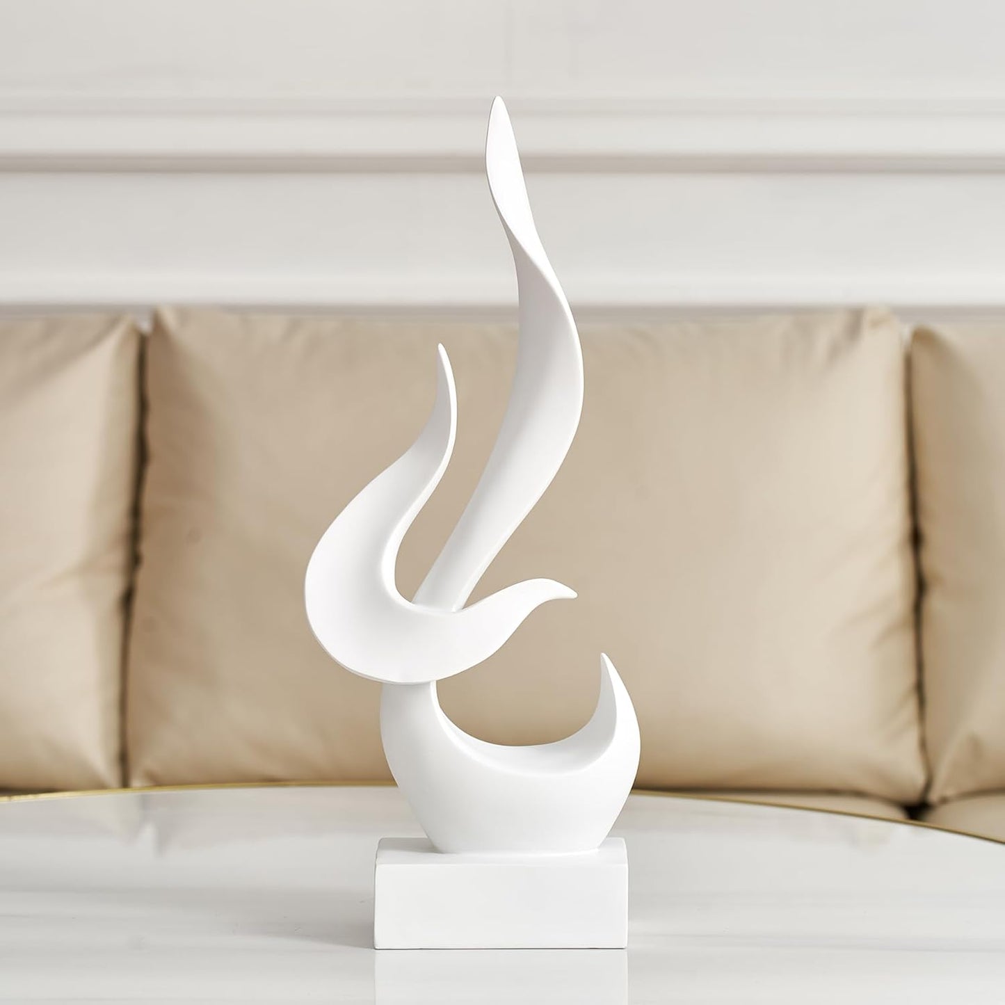 White abstract sculpture on a white surface with a beige sofa in the background