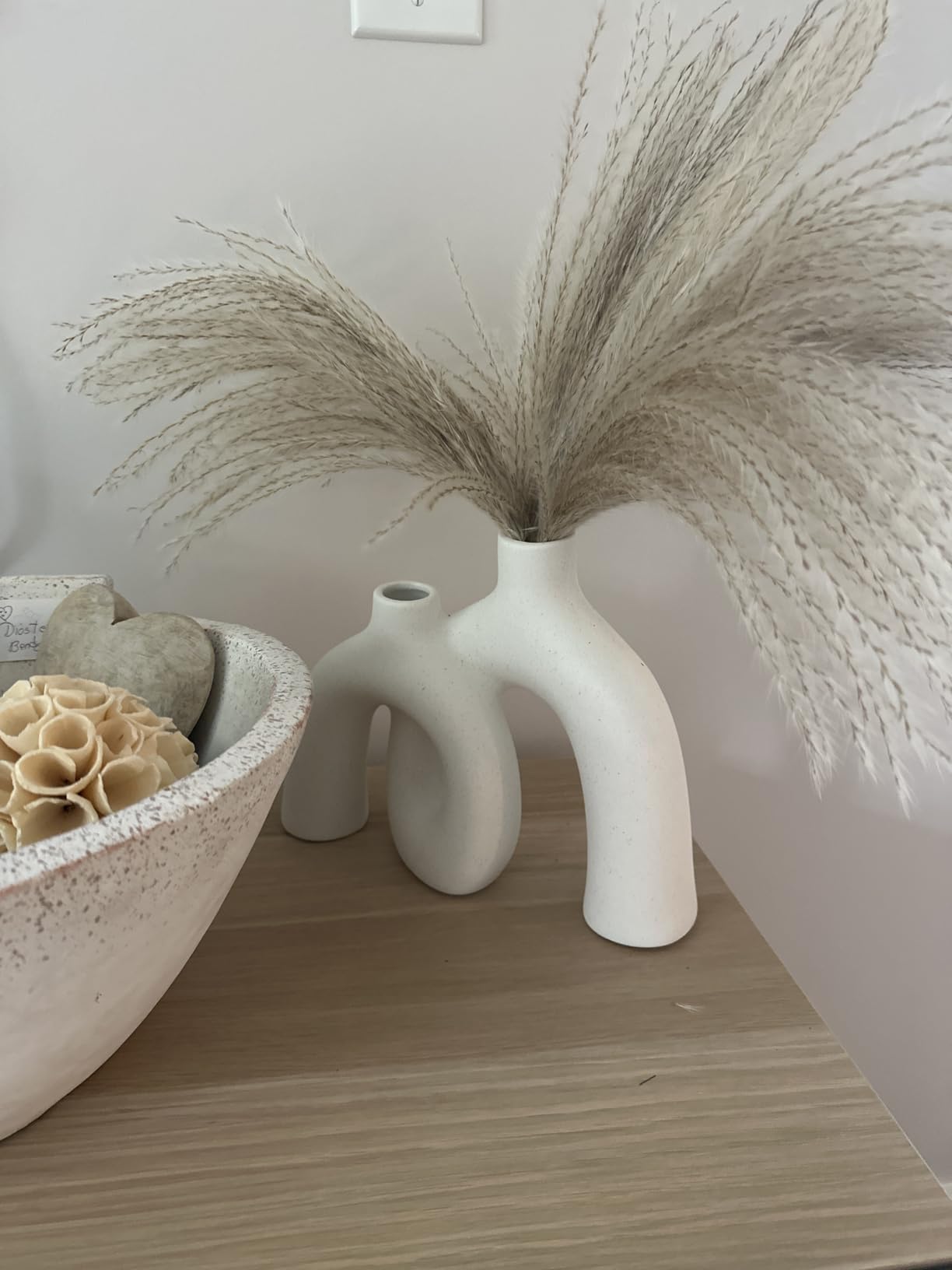 White abstract vase with dried grasses on a wooden surface