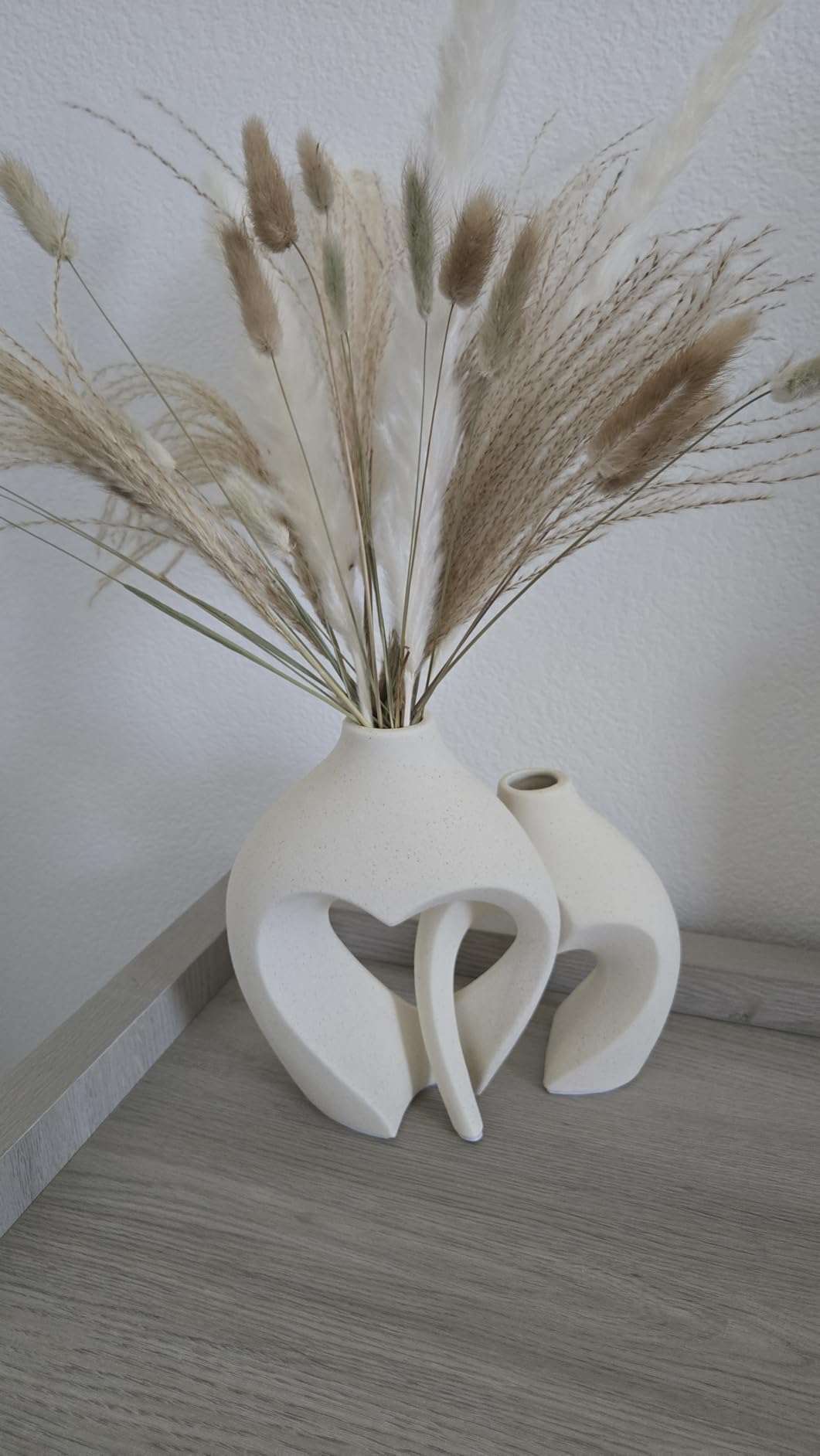 White abstract vase with dried plants on a light wooden floor against a white wall