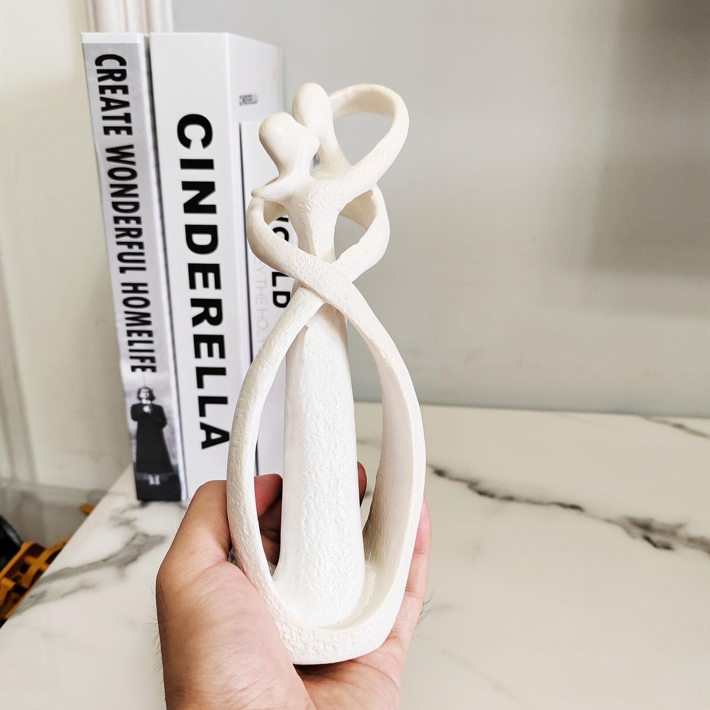 White ceramic sculpture held by a hand with books in the background