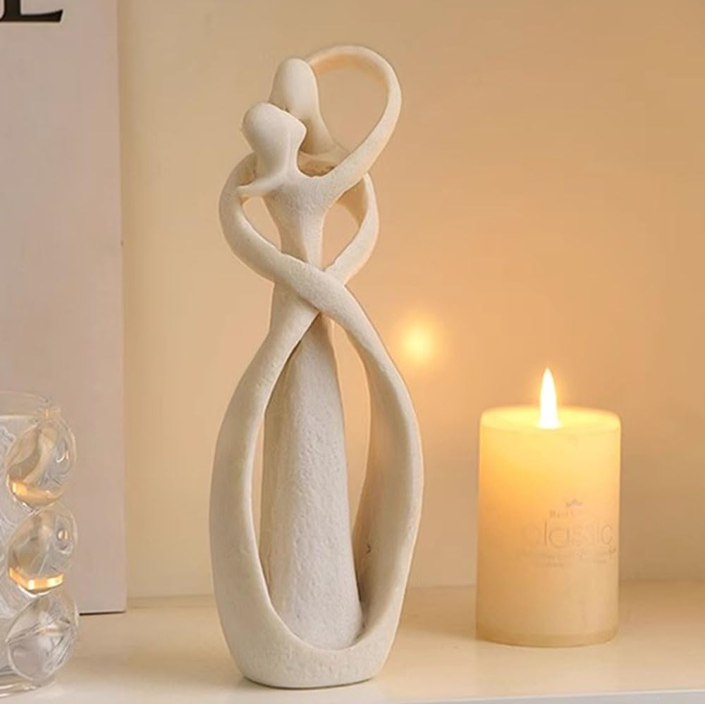 White ceramic sculpture of two intertwined figures on a surface with a lit candle in the background.