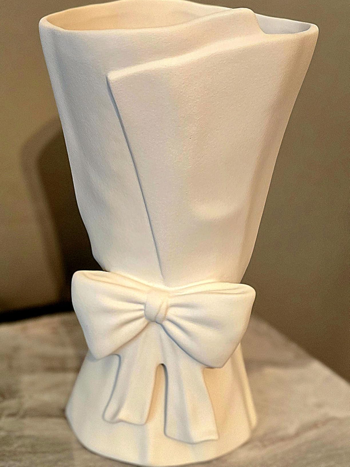 White ceramic vase with a bow design on a neutral background