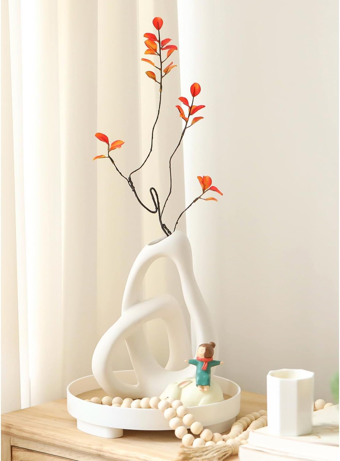 White decorative vase with a branch with red leaves on a wooden surface.