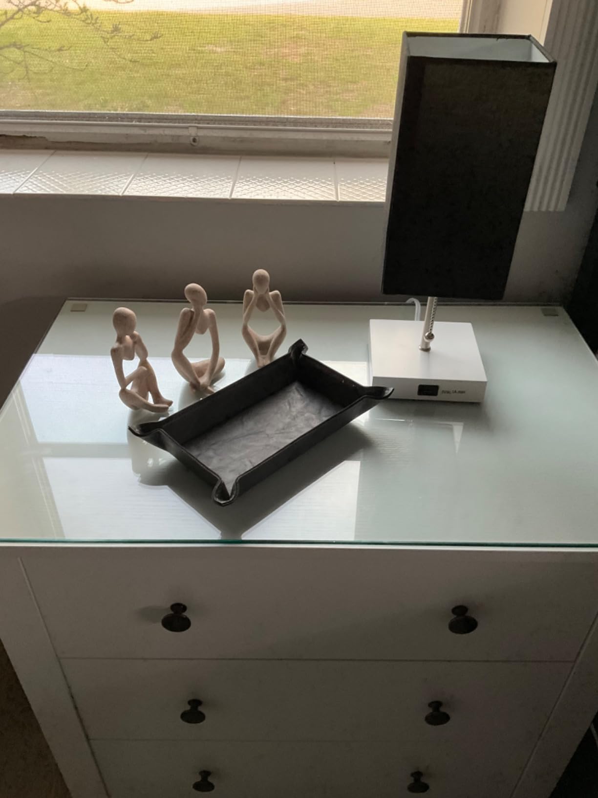 White dresser with glass top displaying decorative items and electronic device.