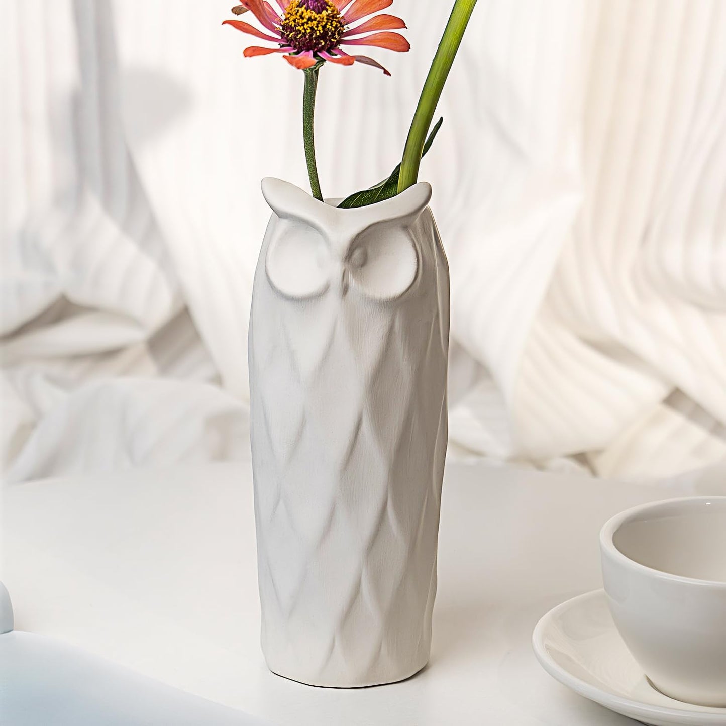 White owl-shaped vase with a flower on a white surface