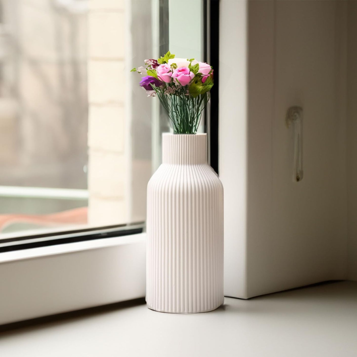 White ribbed vase with pink flowers on a windowsill