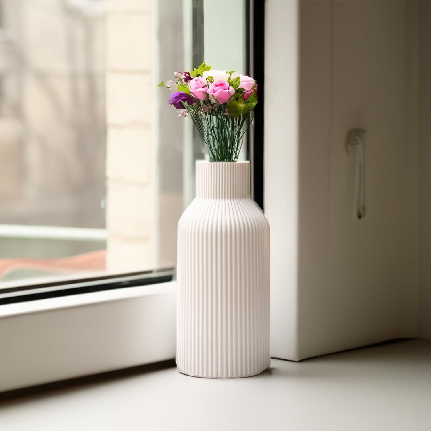 White ribbed vase with pink flowers on a windowsill