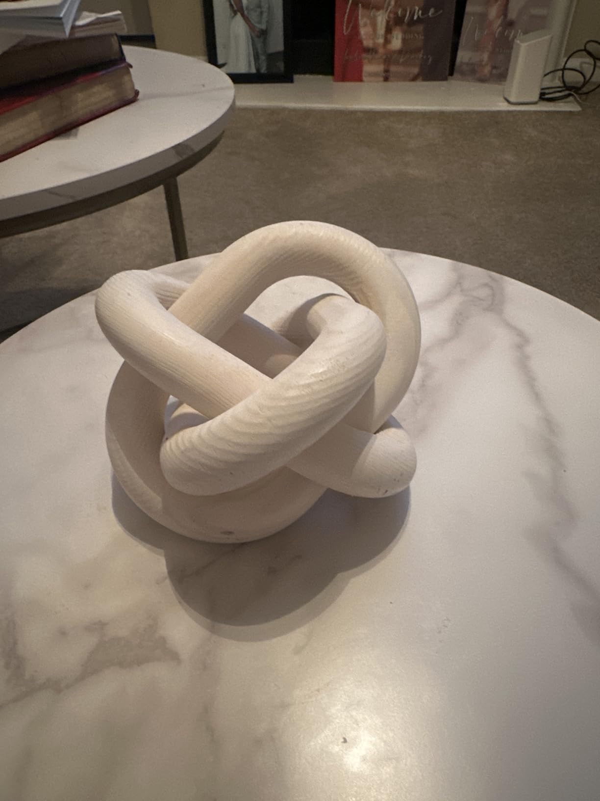 White rope knot sculpture on a marble surface with books and decor in the background