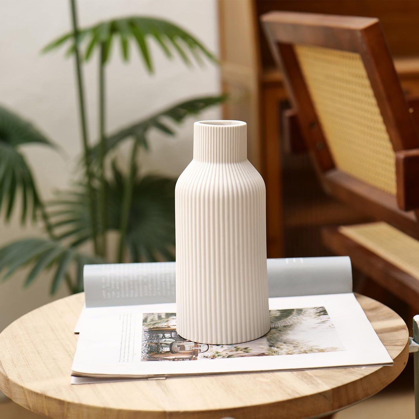 White textured vase on a wooden table with a magazine and plant in the background