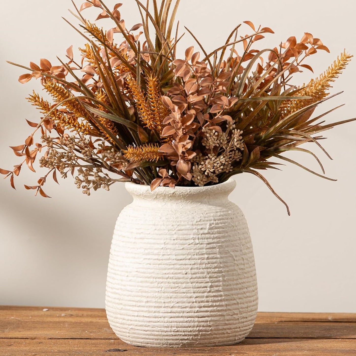 White textured vase with dried plants on a wooden surface