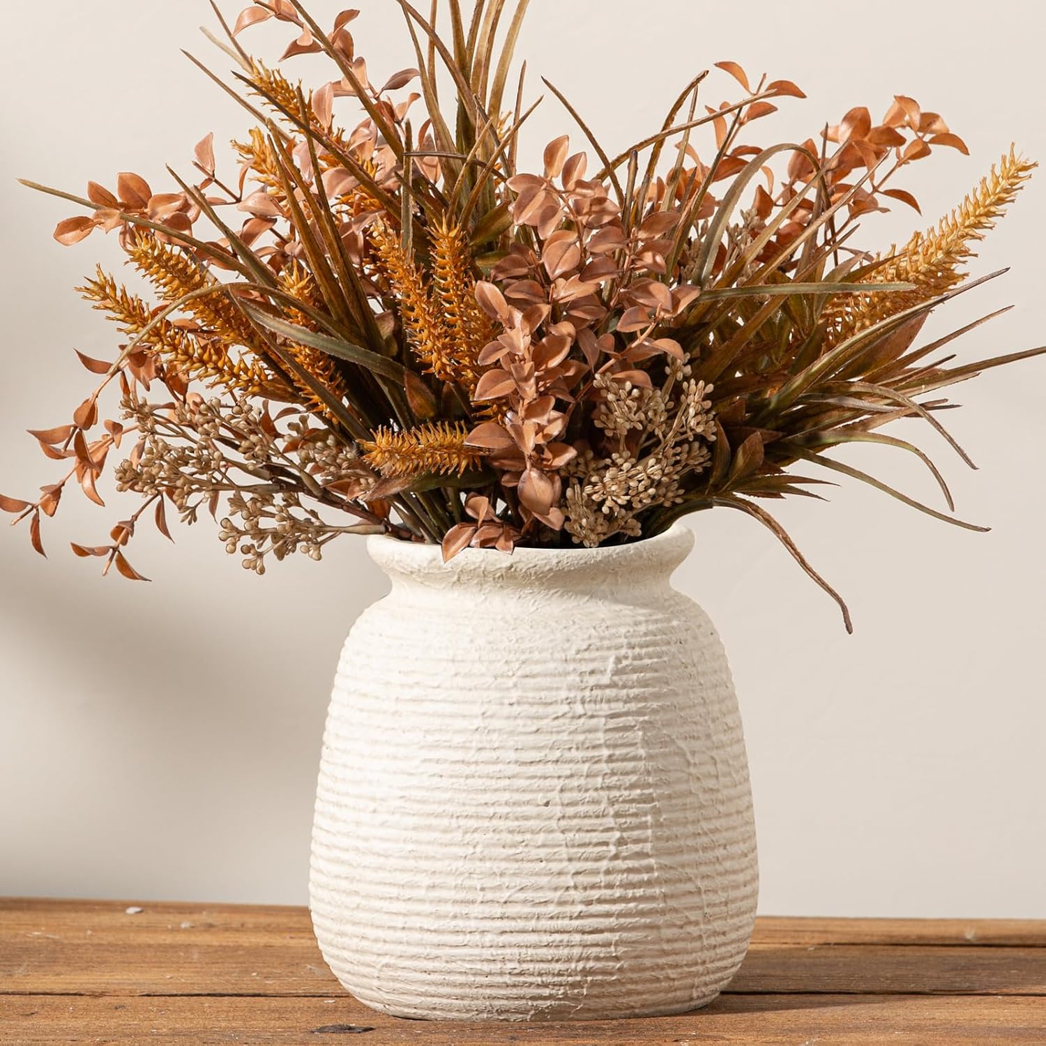 White textured vase with dried plants on a wooden surface
