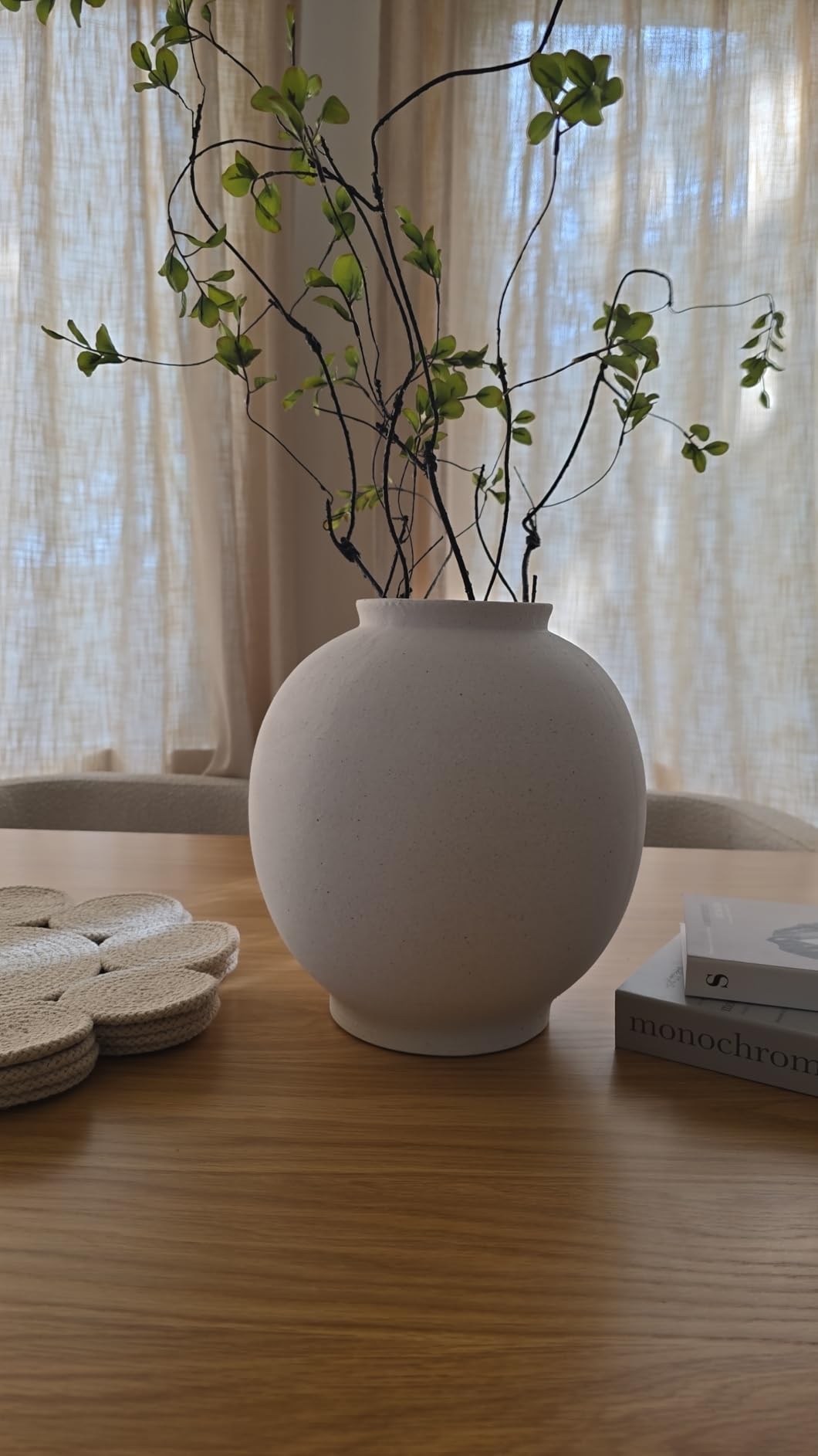White vase with branches on a wooden table with a blurred background