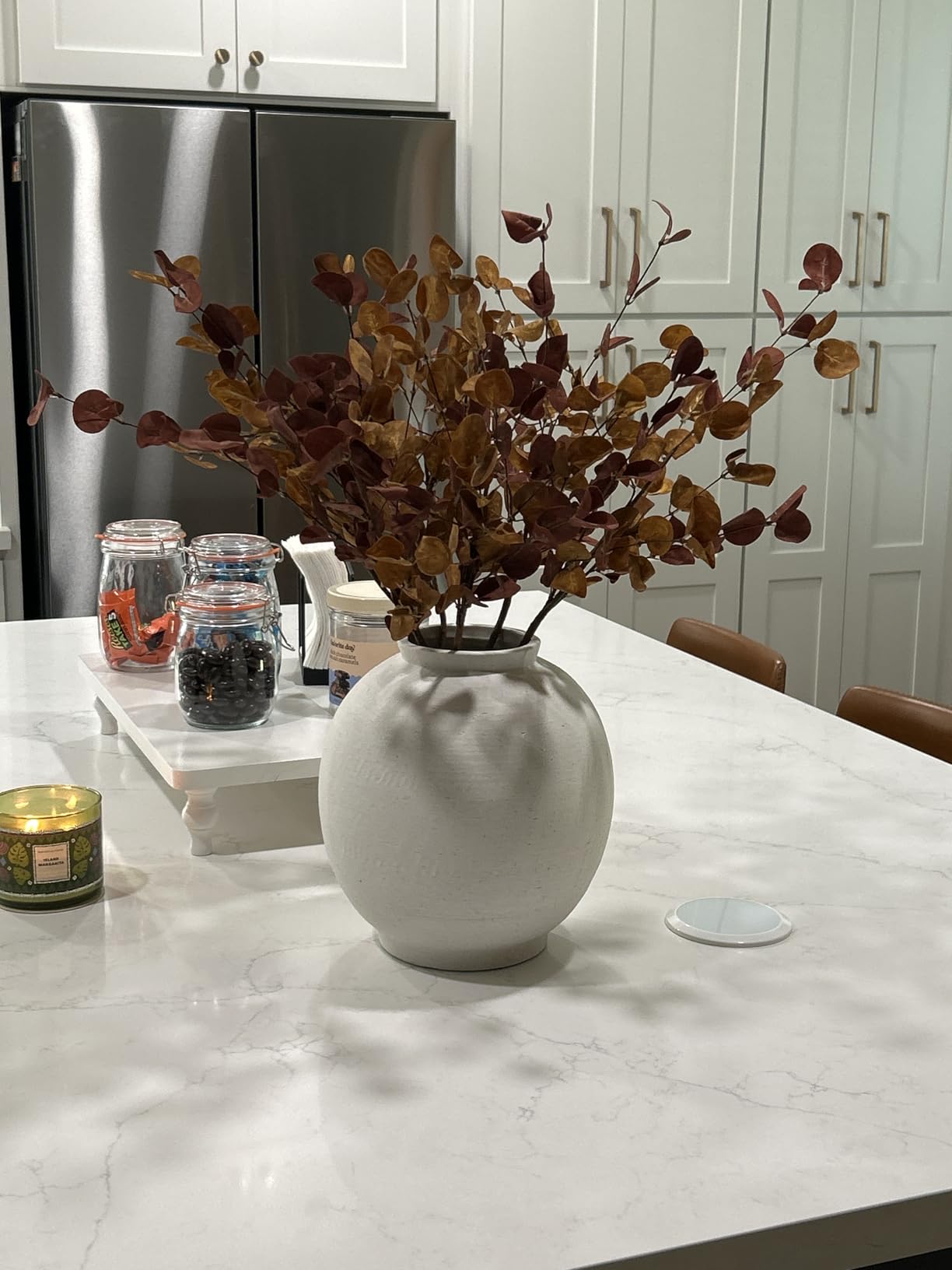 White vase with dried leaves on a marble countertop in a kitchen.