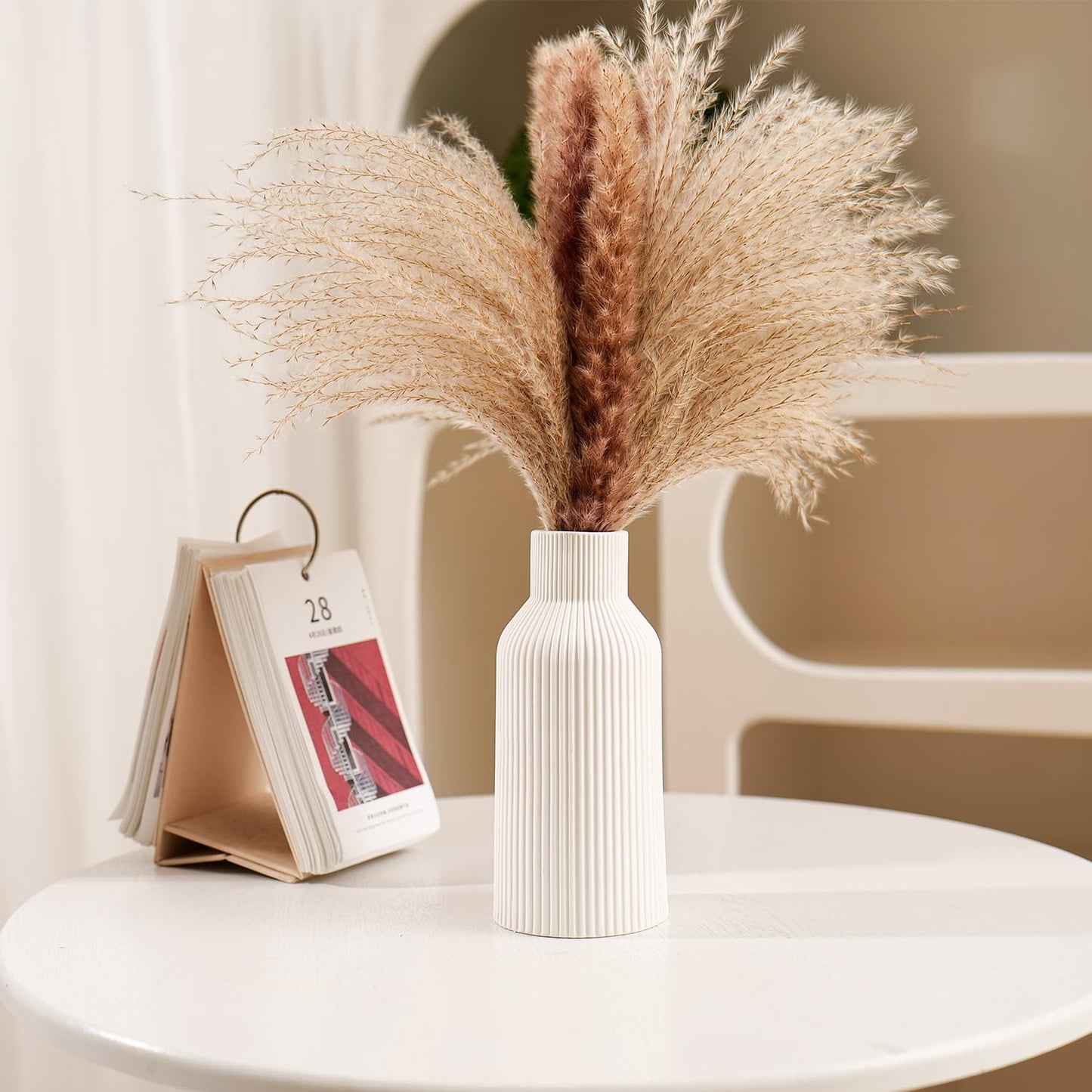 White vase with dried pampas grass on a white surface with a blurred background