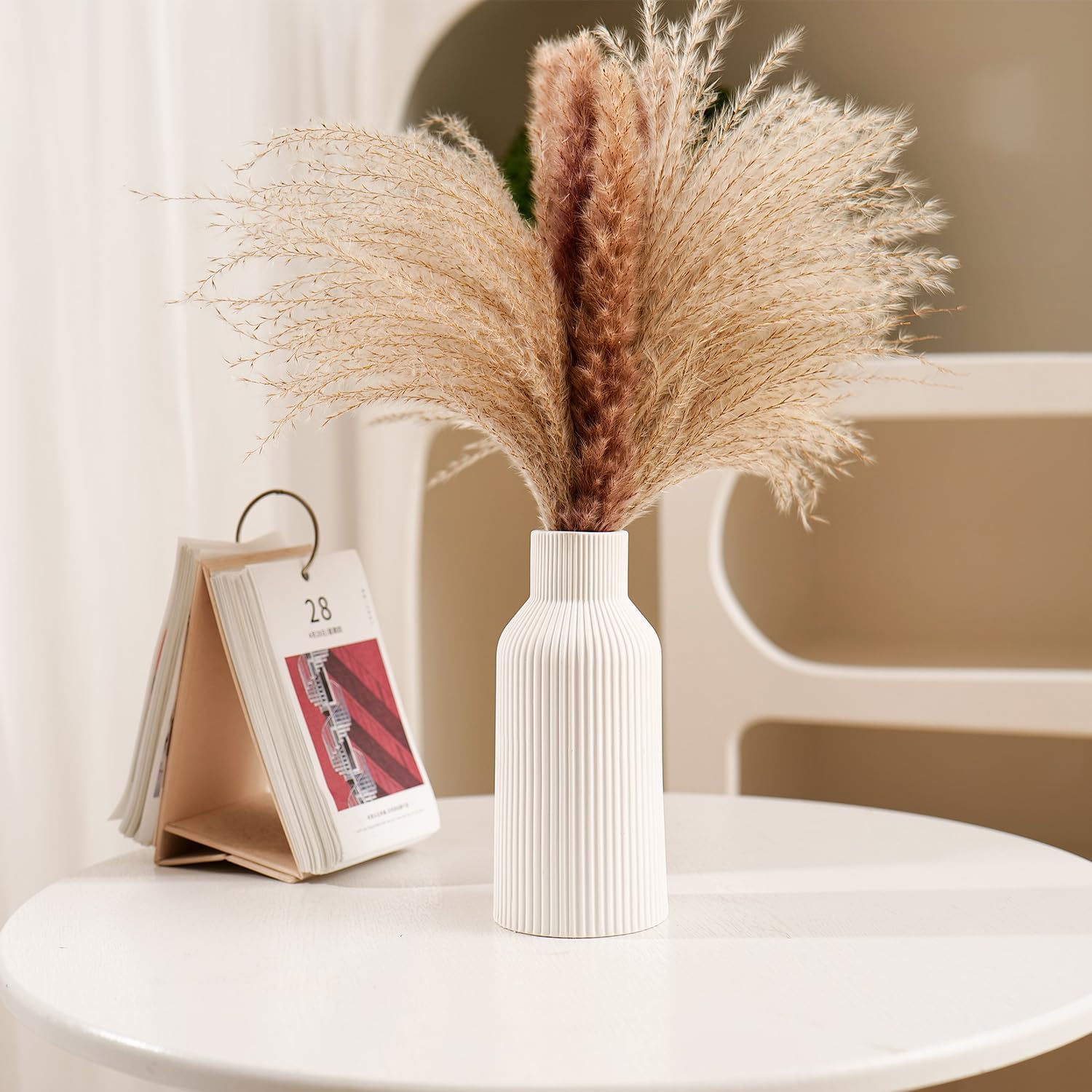 White vase with dried pampas grass on a white surface with a blurred background