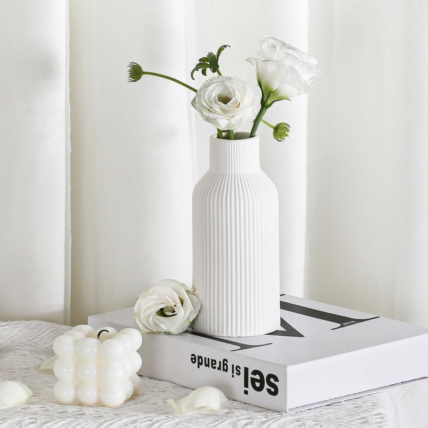 White vase with flowers on a book against a white background