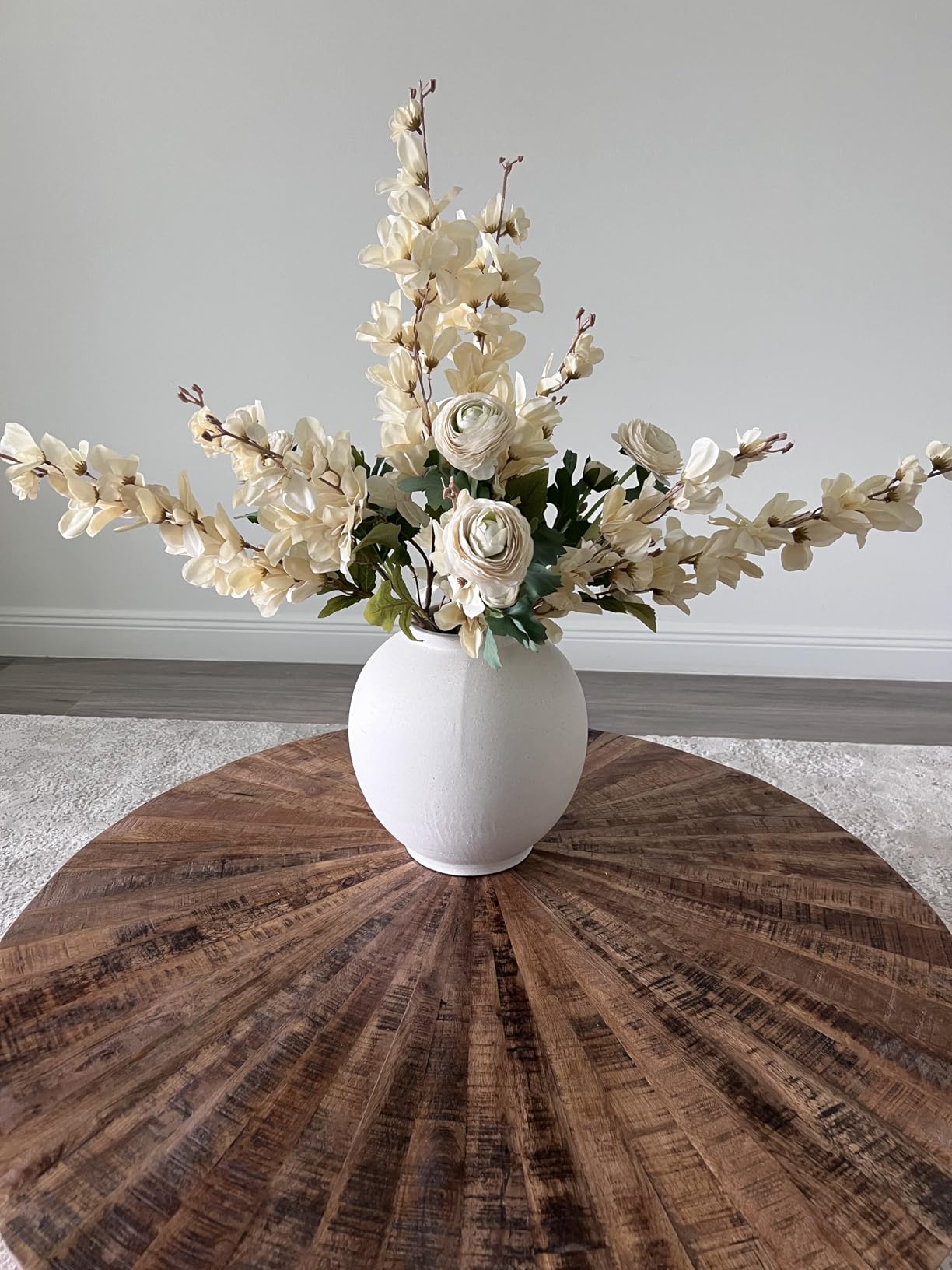 White vase with flowers on a wooden table against a gray wall