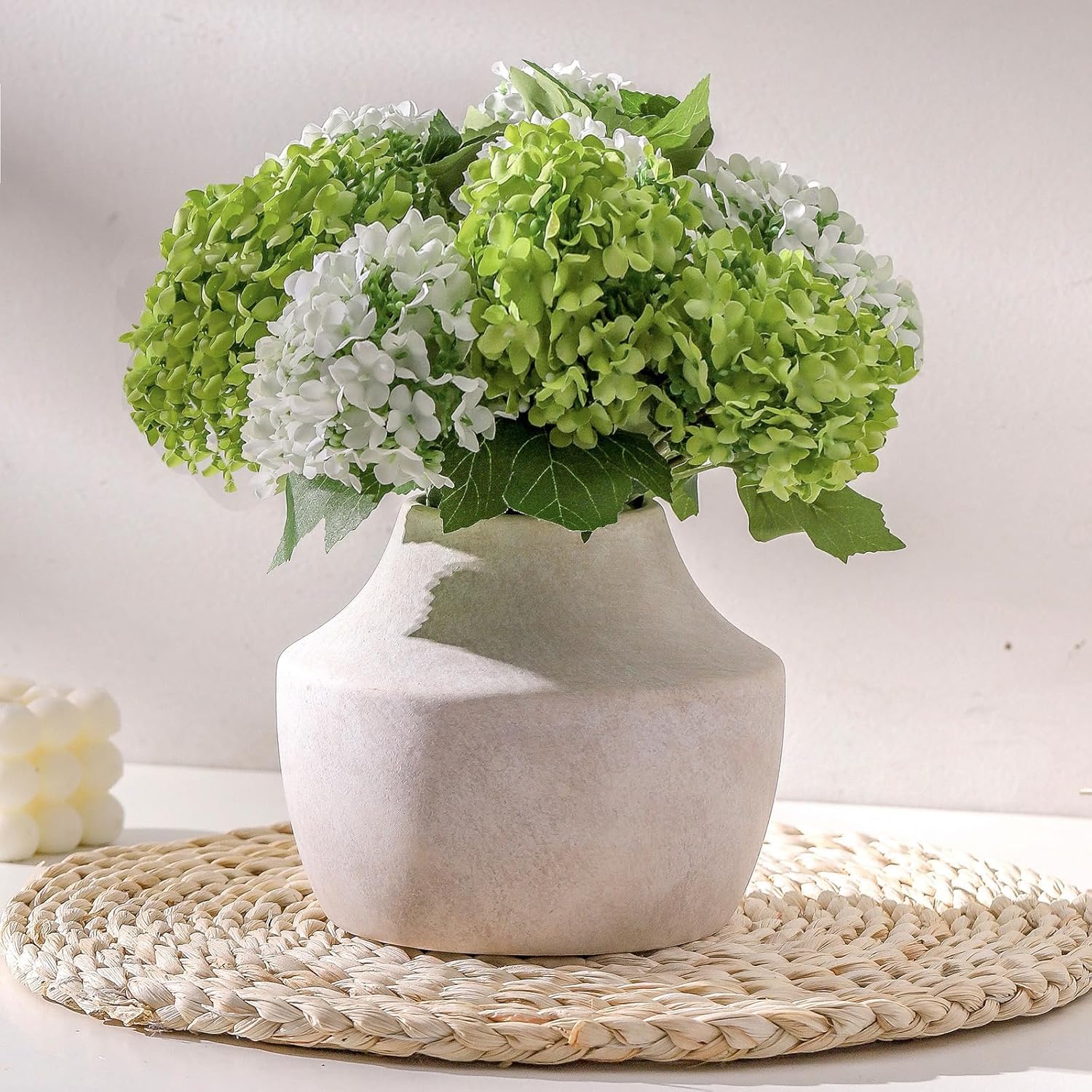 White vase with green and white hydrangeas on a woven mat