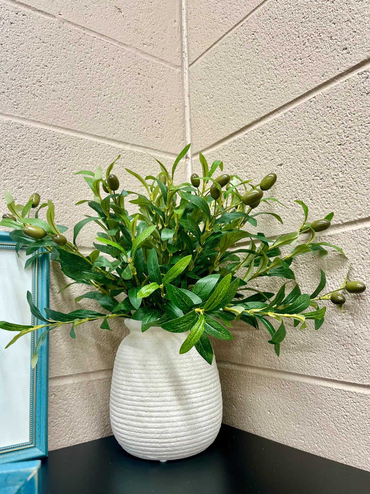 White vase with green plant against a beige wall